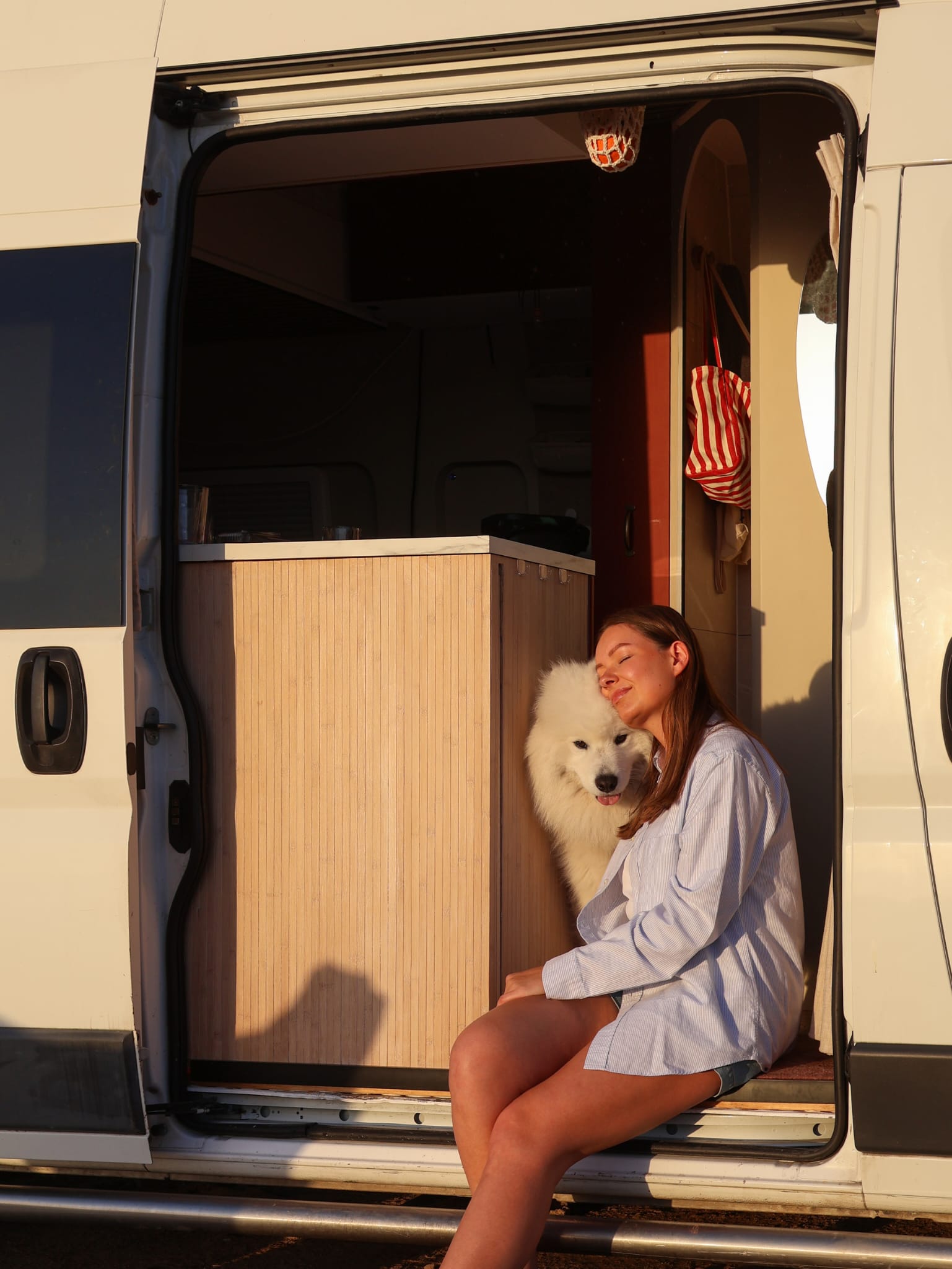 Lotte Boersma in de deuropening van haar camper, knuffelend met haar hond